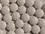 A close-up view of numerous white, round, tablet-like pills with markings '30' and 'M' embossed on them. The pills are arranged in a scattered pattern filling the entire frame.