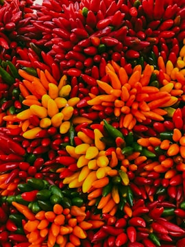 A vibrant and colorful arrangement of various peppers, predominantly in shades of red, orange, yellow, and green. The peppers are closely packed together, creating a striking visual display full of texture and color.