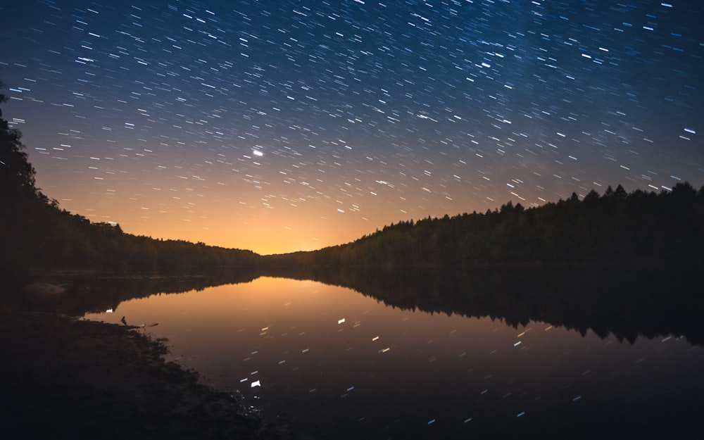 a lake with trees and a starry sky above