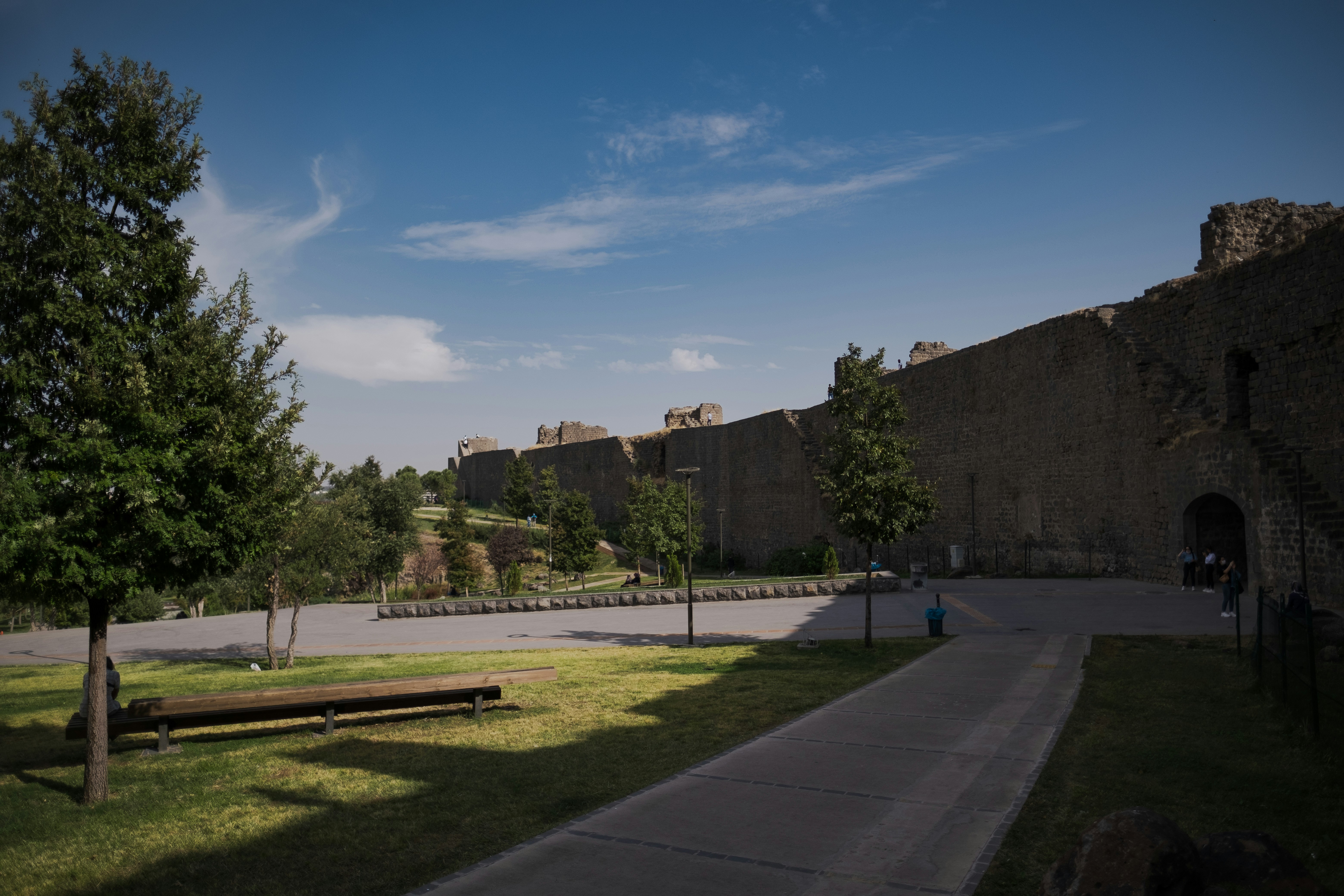 a road with grass and trees by a stone wall and a road