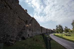 a stone wall with a walkway and grass and trees