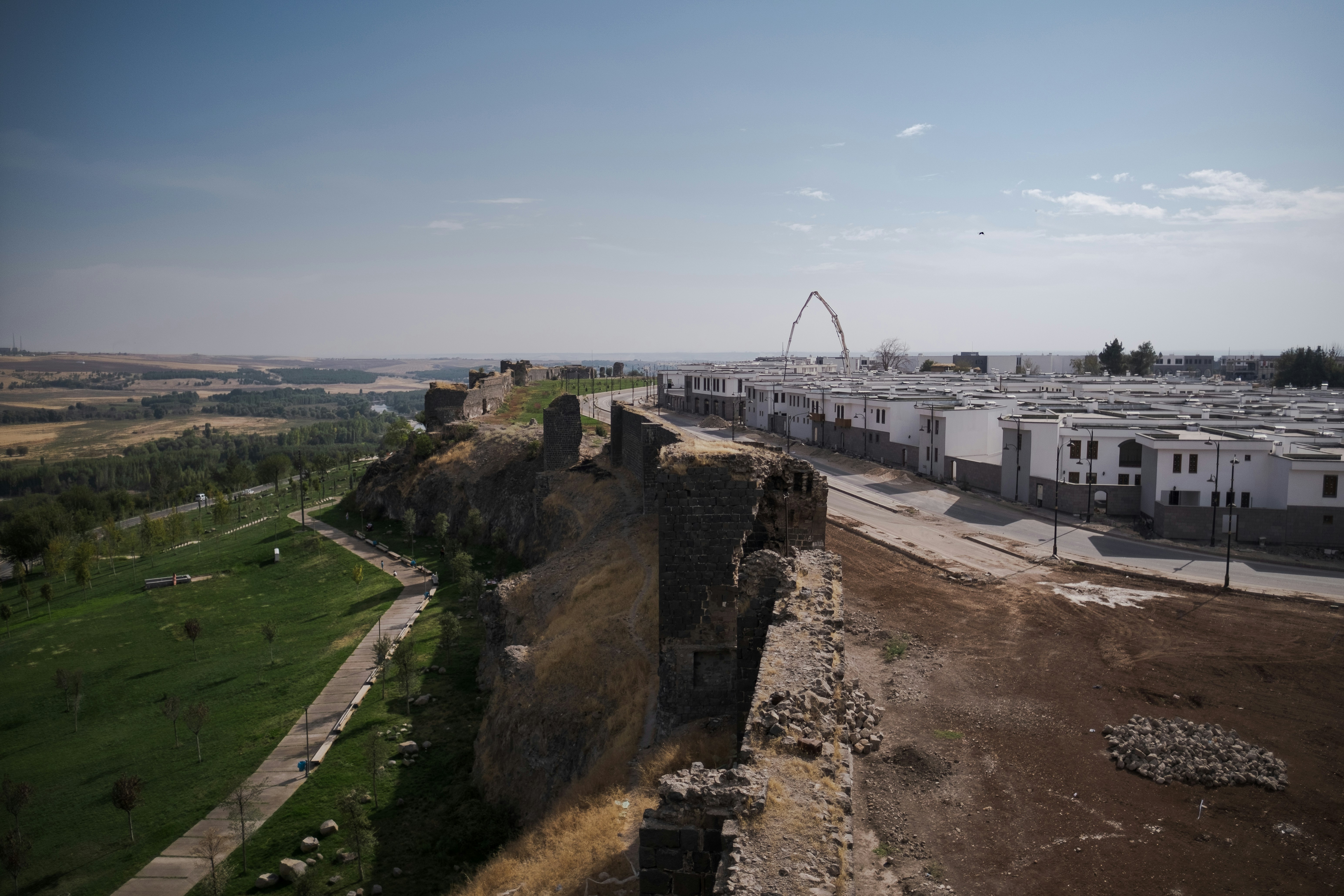 a large stone wall with a grass field and buildings in the background