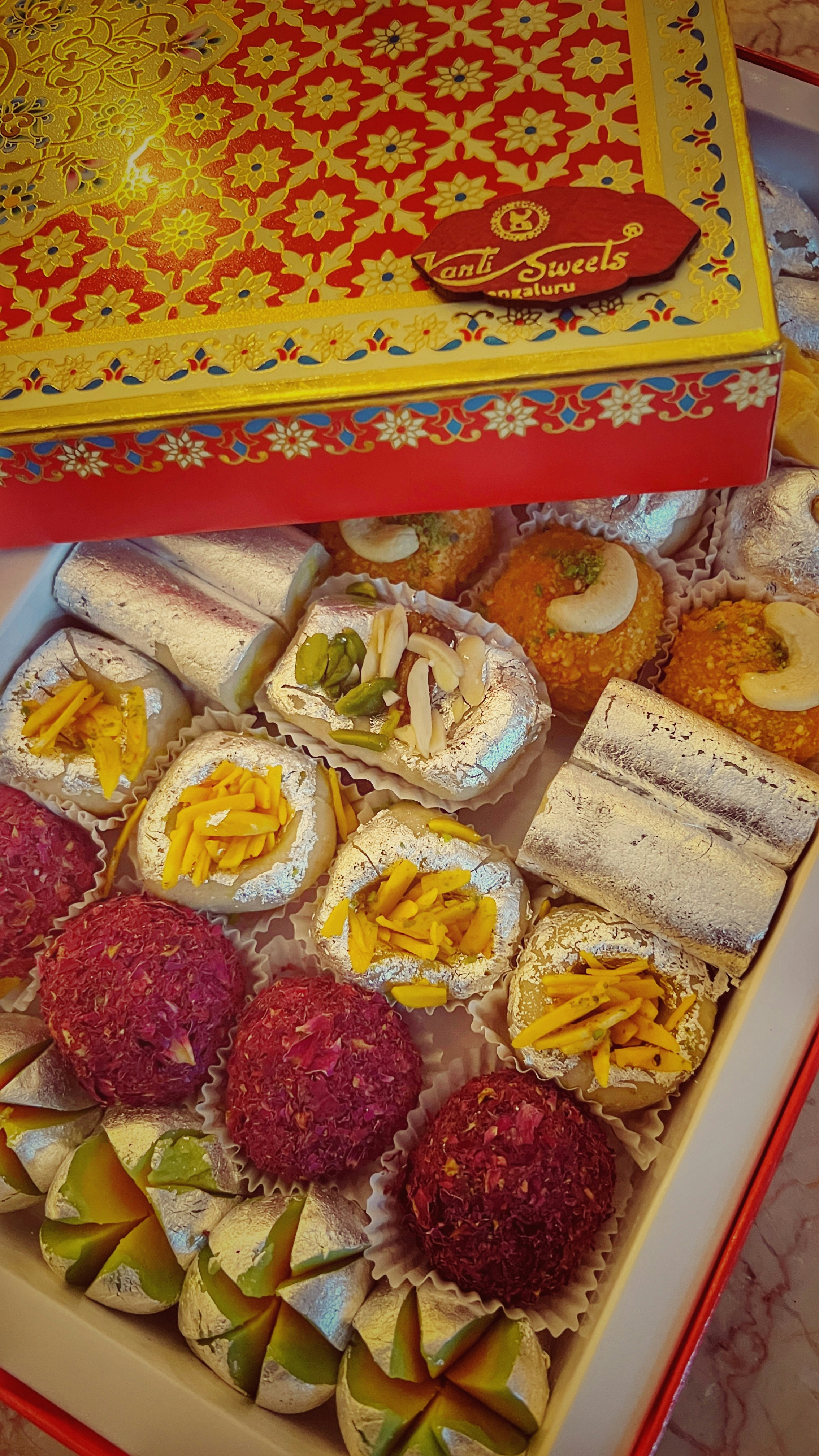 Traditional Indian mithai assortment in gold-lined box on white background