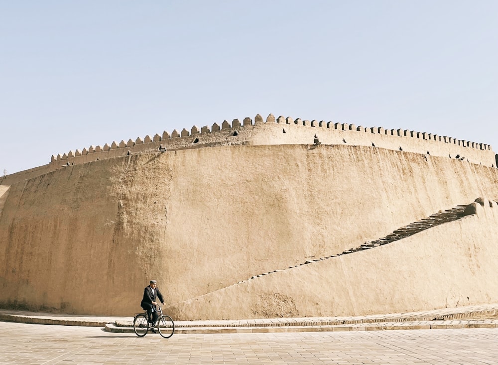 a person riding a bike in front of a large stone wall