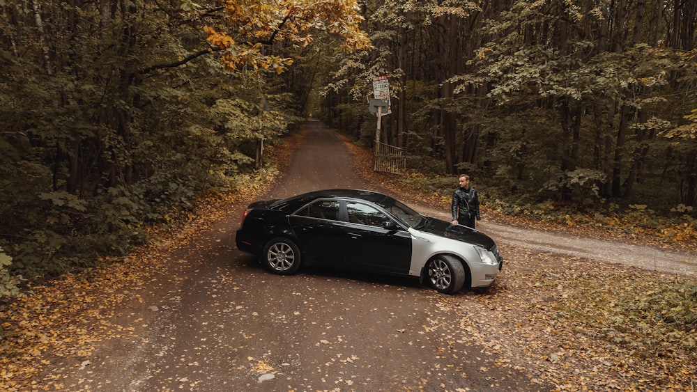 a person standing next to a car on a dirt road surrounded by trees