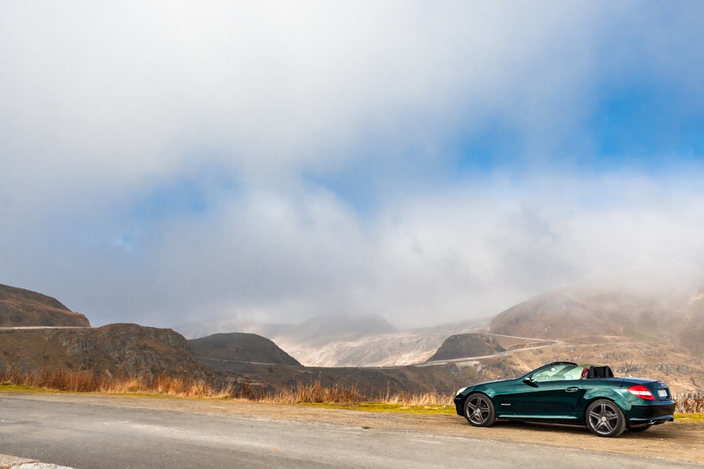 a green car on a road with mountains in the background