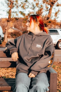 A cozy hoodie with a bold graphic print laid out on a wooden bench surrounded by autumn leaves.