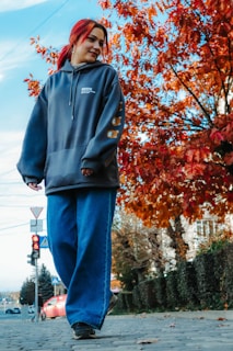 A person wearing a bright red hoodie walking through a city street in autumn