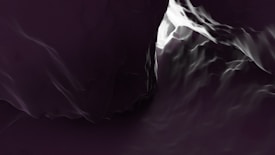 Abstract dark scene with flowing forms resembling waves or liquid, illuminated by contrasting areas of light and shadow. The texture appears smooth with a glossy finish, creating a mysterious and dynamic visual effect.