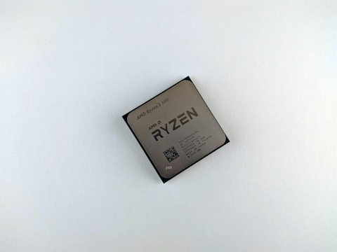 A computer processor with visible branding and specifications printed on its surface. The text includes 'AMD Ryzen 3 3100' along with other technical details and a QR code.