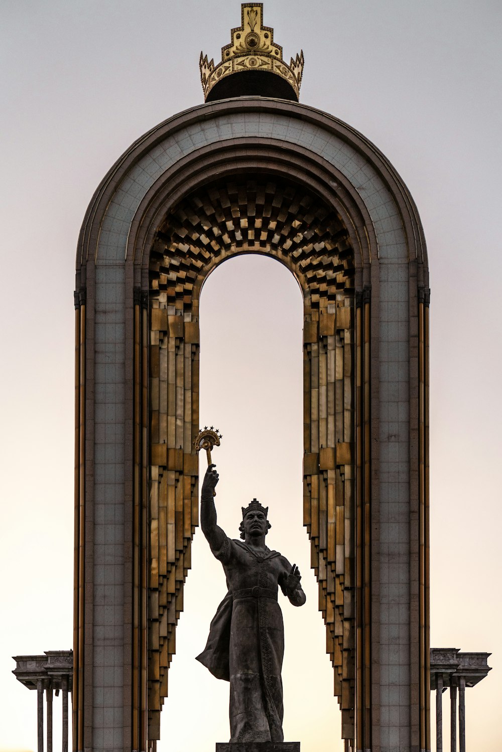 une statue d’une personne tenant une torche devant une grande arche de pierre