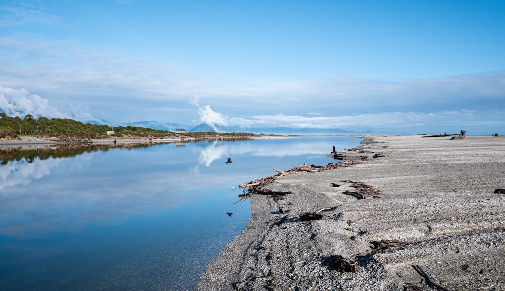 a rocky beach with a body of water and a blue sky