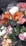 Several bouquets of colorful flowers are wrapped in transparent plastic, displayed in a metal container. The bouquets include a variety of flowers such as pink roses, orange gerberas, white chrysanthemums, and yellow daisies, creating a vibrant assortment.