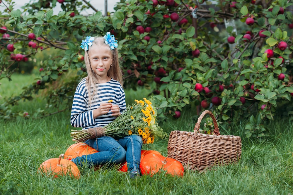 a girl sitting in a field of pumpkins and a basket of flowers