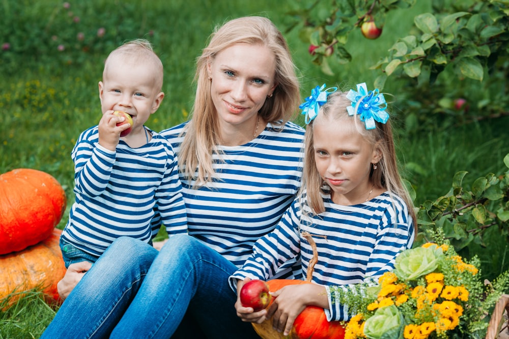 a person and two children sitting on grass with pumpkins and flowers