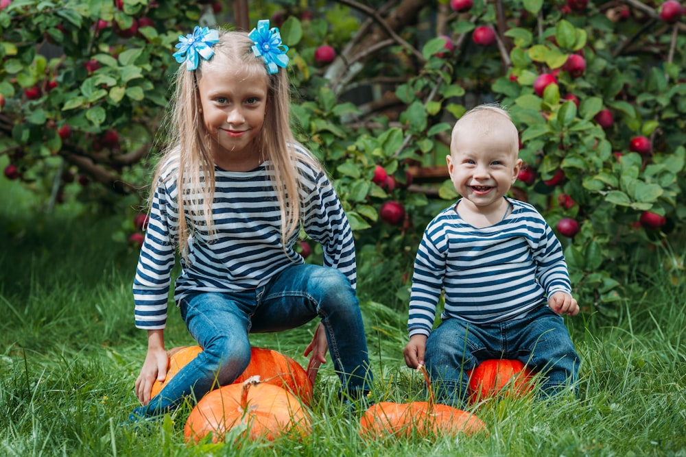 a boy and girl sitting on a pumpkin in a yard