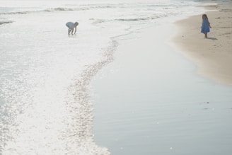 Children playing on a sandy beach with gentle waves in the background.