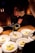 A chef is carefully plating dishes under warm lighting. Each white plate is topped with ravioli in a creamy sauce and garnished with fresh herbs. The chef uses a spoon to add sauce with precision, demonstrating attention to detail and culinary skill.
