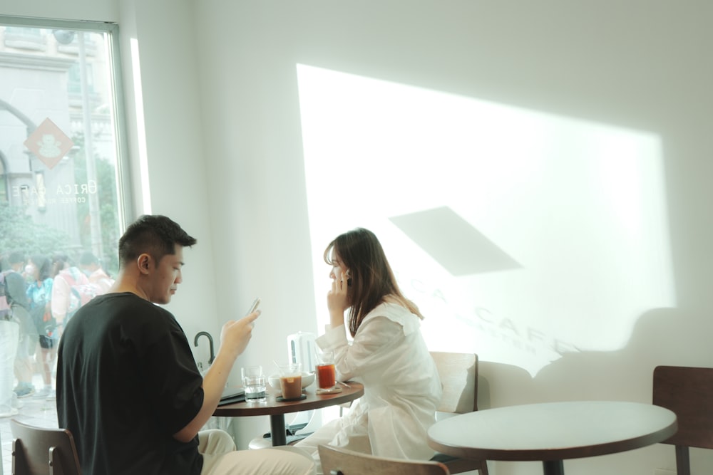 a man and woman sitting at a table in a room with a window