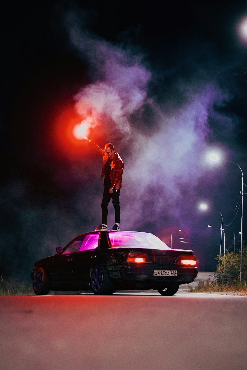 a person standing on the back of a car with a fire behind him
