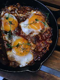 Close-up of a cast iron skillet sizzling with a golden breakfast hash topped with fresh herbs