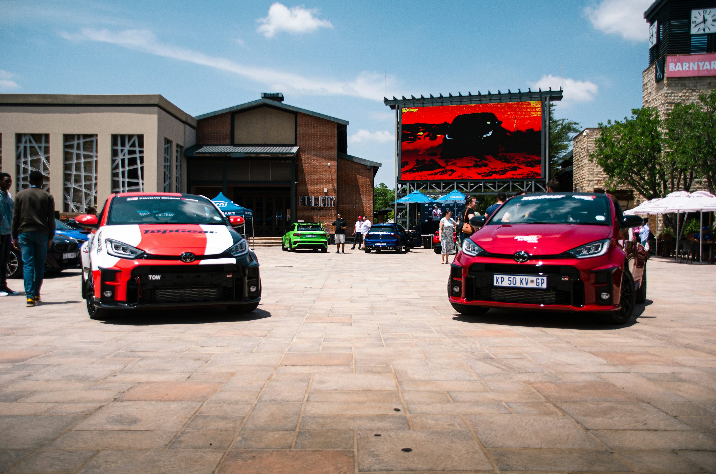 a couple of cars parked in a parking lot with people and buildings in the background
