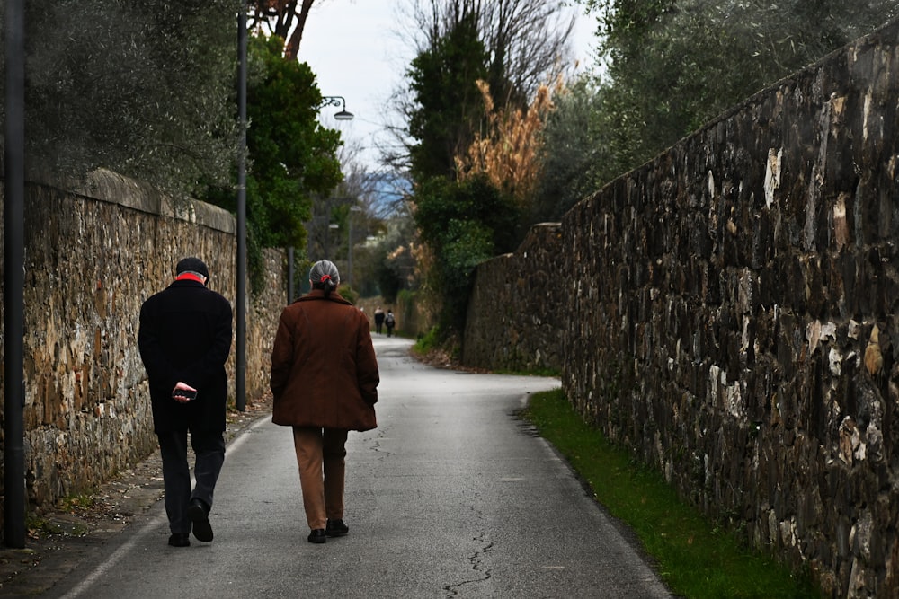 a couple of people walking down a road between stone walls