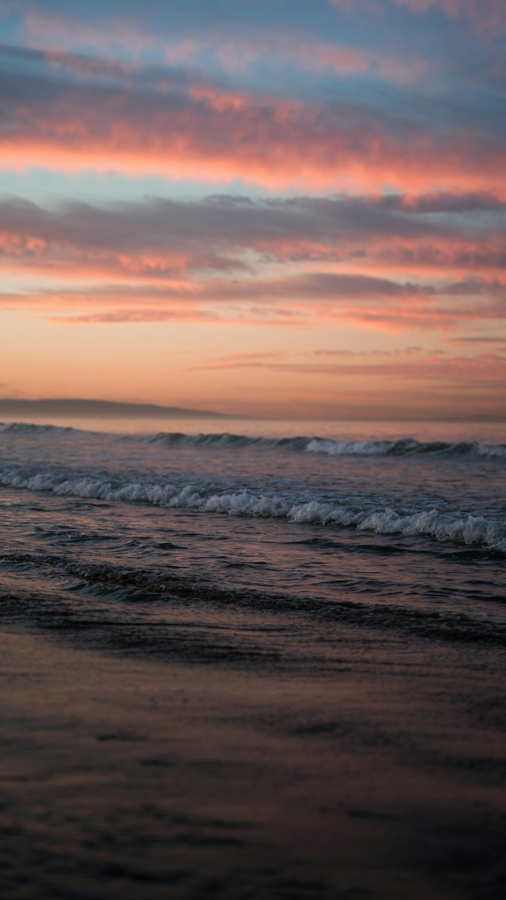 a beach with waves and a pink and purple sky