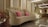 A luxurious sofa adorned with pink cushions is surrounded by a lavish arrangement of white and pink flowers. The setting features elegant lighting with ceiling fixtures, creating a sophisticated atmosphere. The background includes a decorated panel and an electronic keyboard, suggesting an event space.