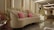 A luxurious sofa adorned with pink cushions is surrounded by a lavish arrangement of white and pink flowers. The setting features elegant lighting with ceiling fixtures, creating a sophisticated atmosphere. The background includes a decorated panel and an electronic keyboard, suggesting an event space.