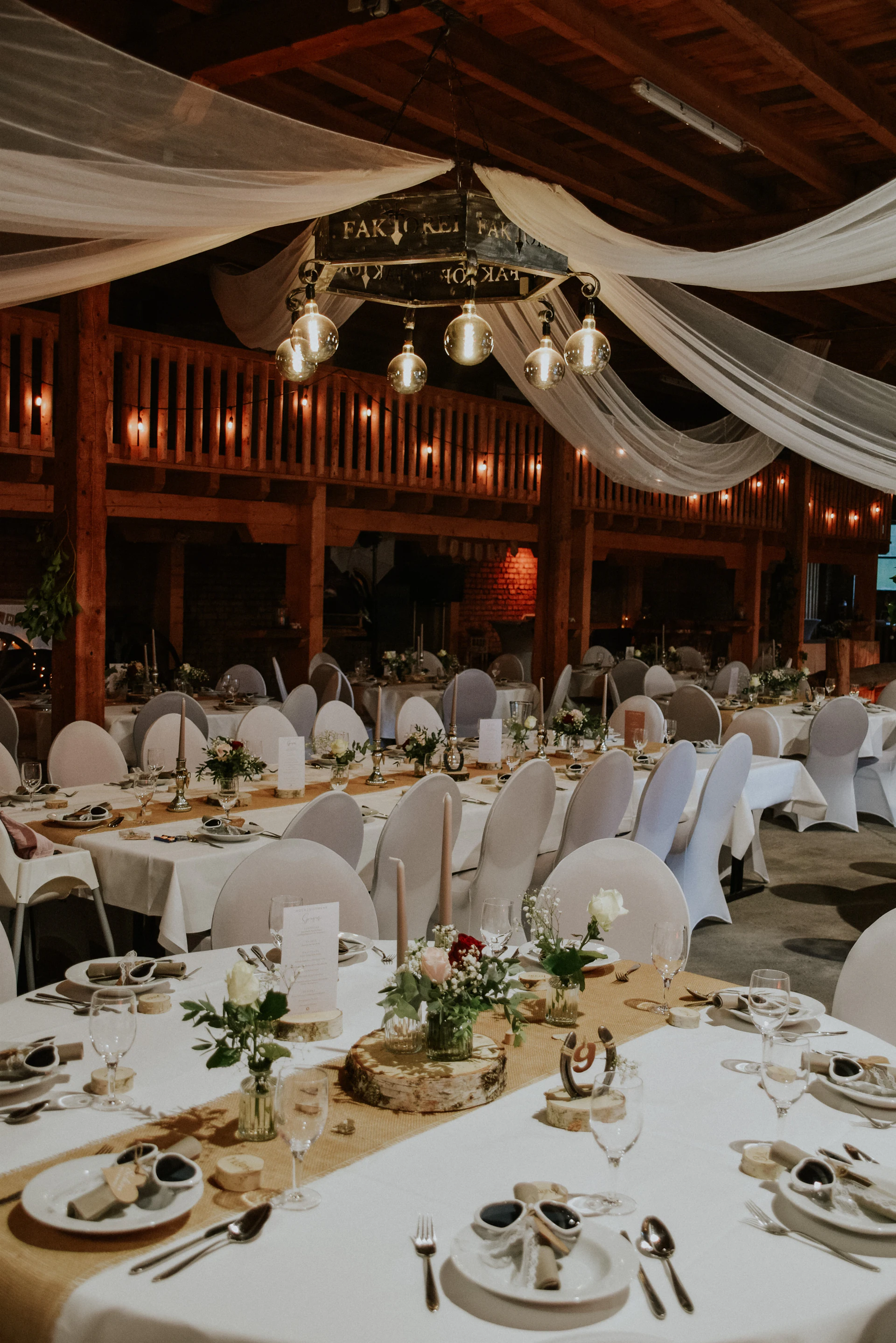Restored beamed barn reception with white draping, long tables and warm string lights