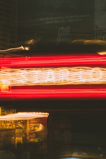Neon lights create a dynamic blur of red and yellow colors, with visible text above offering motivational phrases. The lights suggest a storefront or a bar, with a lively atmosphere. Background elements include posters or signage, partially visible through the motion.