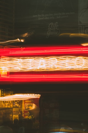 Neon lights create a dynamic blur of red and yellow colors, with visible text above offering motivational phrases. The lights suggest a storefront or a bar, with a lively atmosphere. Background elements include posters or signage, partially visible through the motion.