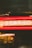 Neon lights create a dynamic blur of red and yellow colors, with visible text above offering motivational phrases. The lights suggest a storefront or a bar, with a lively atmosphere. Background elements include posters or signage, partially visible through the motion.