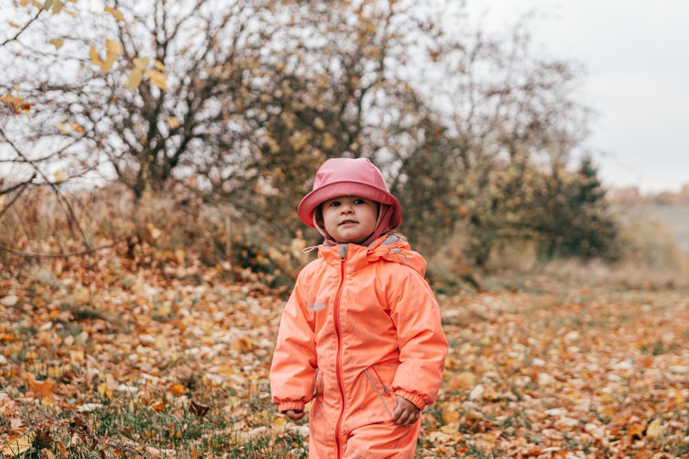 a child wearing a pink jacket and standing in a field of grass