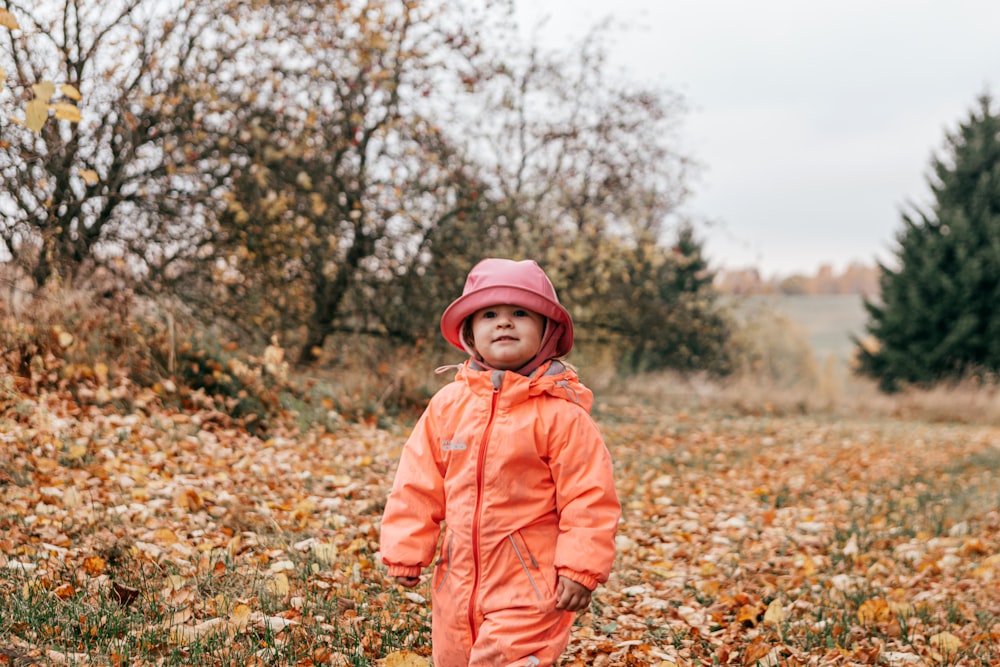 a child wearing a red jacket and standing in a field of leaves