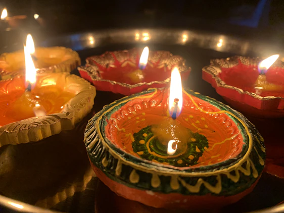 A cozy scene with glowing handcrafted diyas arranged alongside vibrant sarees and kurtis, bathed in warm festival light.