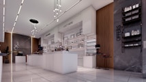 A modern, well-lit retail space with sleek white display counters and shelves. The ceiling features contemporary lighting fixtures, and the space incorporates wood and stone accents. Products are neatly arranged on the shelves, and promotional signs are visible.