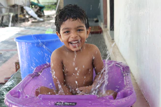 A joyful child splashing water while sitting in a sky blue inflatable pool with rounded edges.