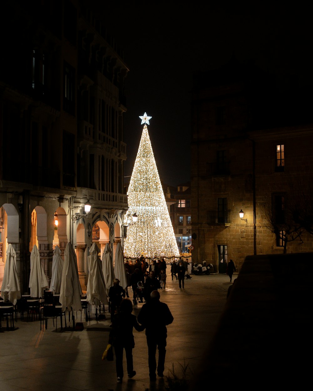 people walking on a street with a large christmas tree in the middle