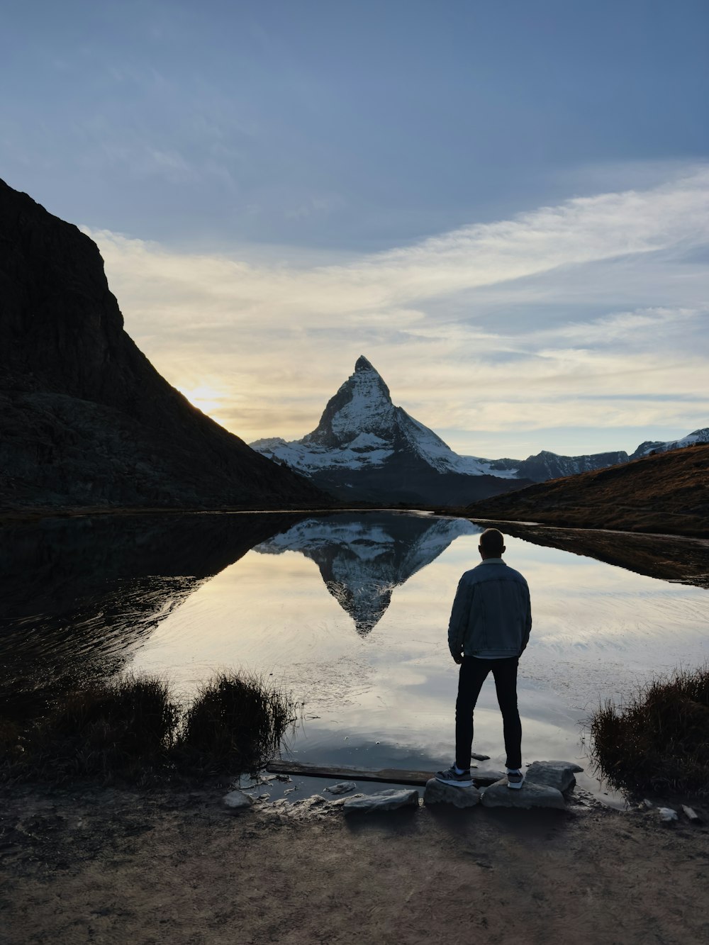 a man standing on a rock in front of a lake with a mountain in the background