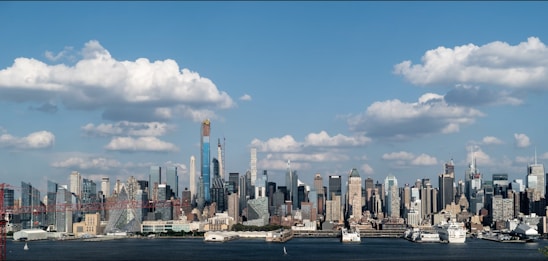 A panoramic view of a modern city skyline with cranes and construction sites under a clear blue sky.