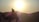 A silhouette of a person riding a camel with a bright sun setting behind distant hills, creating a serene and peaceful scene.