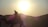A silhouette of a person riding a camel with a bright sun setting behind distant hills, creating a serene and peaceful scene.