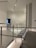 An interior space with modern architecture, featuring clean lines and minimalistic design. The area includes a railing alongside a path, illuminated by overhead lighting. The walls are adorned with subtle text or art, adding to the contemporary feel.