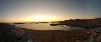 A panoramic sunset view over a serene coastal landscape with warm golden hues reflecting on the water.