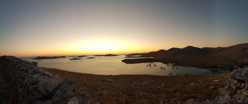 A panoramic sunset view over a serene coastal landscape with warm golden hues reflecting on the water.