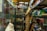 A cluttered room filled with various items on display, including a mannequin torso and a headless mannequin, shelves full of boxes, toys, and collectibles. The space is cramped with items stacked haphazardly on shelves and in glass cabinets. There is a mix of old electronics, model cars, and other vintage memorabilia.