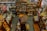 An overhead view of a cluttered antique store filled with various items. Shelves are stocked with vintage pottery, teapots, and glassware, while tables display decorative plates, vases, and lamps. There are wooden furniture pieces, small baskets, and books scattered throughout the space. A variety of eclectic and nostalgic objects create a sense of organized chaos.