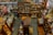 An overhead view of a cluttered antique store filled with various items. Shelves are stocked with vintage pottery, teapots, and glassware, while tables display decorative plates, vases, and lamps. There are wooden furniture pieces, small baskets, and books scattered throughout the space. A variety of eclectic and nostalgic objects create a sense of organized chaos.
